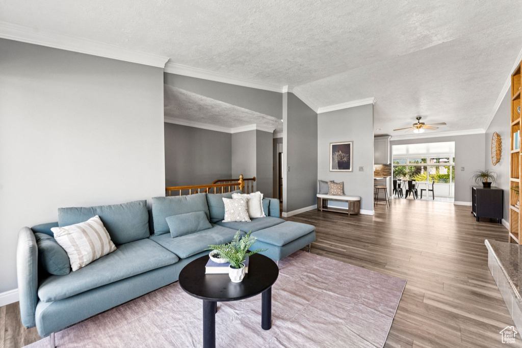 Living room featuring a ceiling fan, wood finished floors, a textured ceiling, lofted ceiling, and crown molding