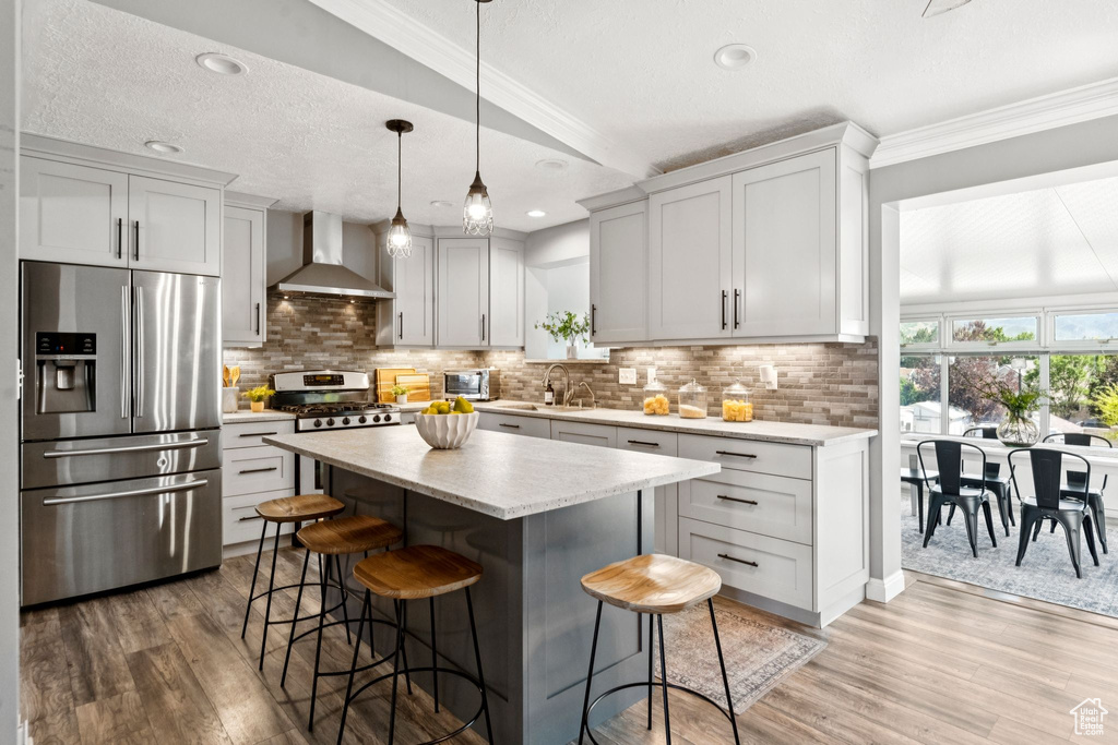 Kitchen with stainless steel appliances, wall chimney exhaust hood, a breakfast bar area, light wood-style floors, and ornamental molding