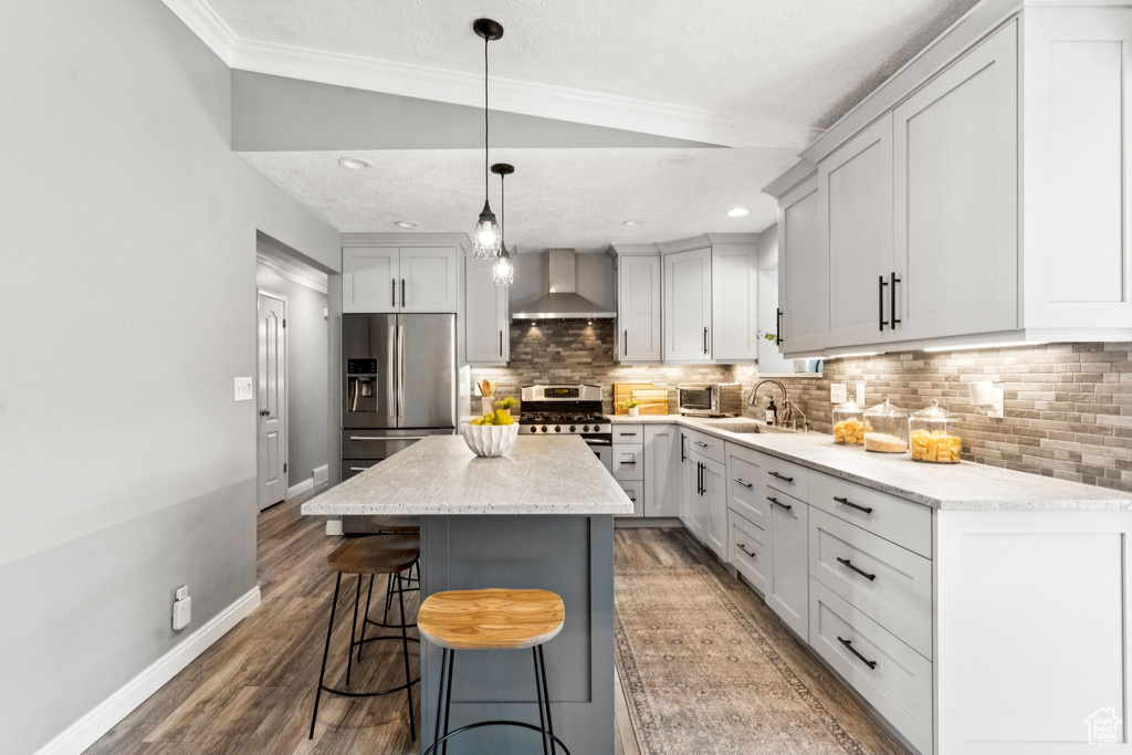 Kitchen with wall chimney range hood, stainless steel appliances, backsplash, a kitchen breakfast bar, and a kitchen island