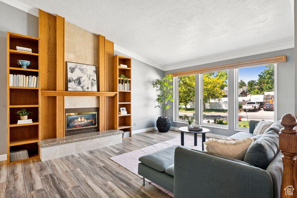 Living room with a textured ceiling, a tile fireplace, wood finished floors, ornamental molding, and built in features