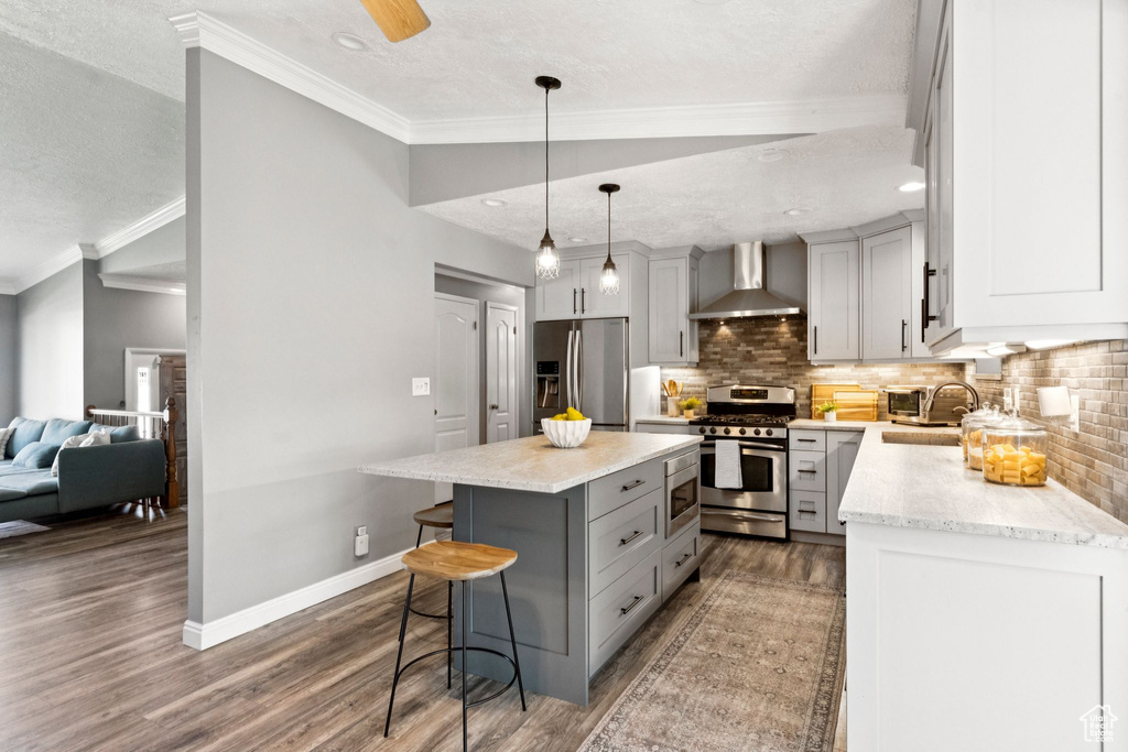 Kitchen with appliances with stainless steel finishes, wall chimney exhaust hood, gray cabinets, a breakfast bar, and decorative backsplash