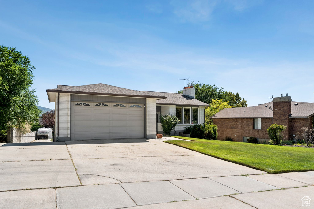 Ranch-style house with brick siding, a garage, driveway, a front yard, and a chimney