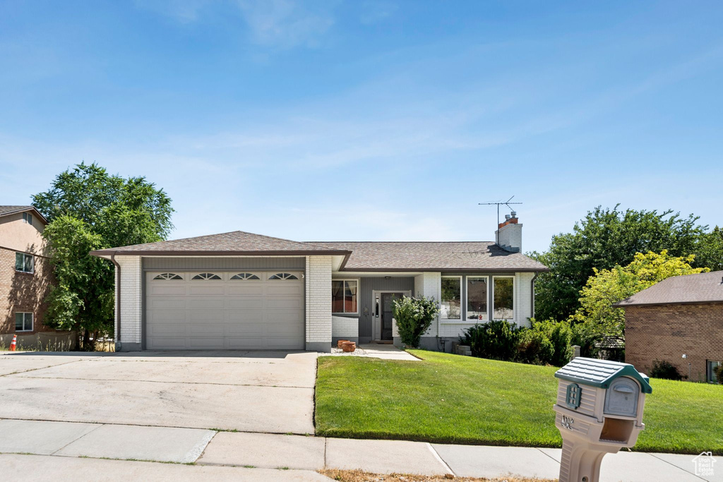 Ranch-style house with a garage, a front yard, driveway, and a chimney