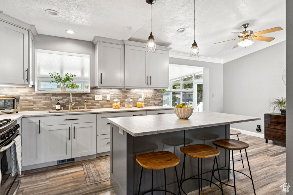 Kitchen featuring stainless steel gas range oven, a breakfast bar area, tasteful backsplash, light wood-style flooring, and a textured ceiling