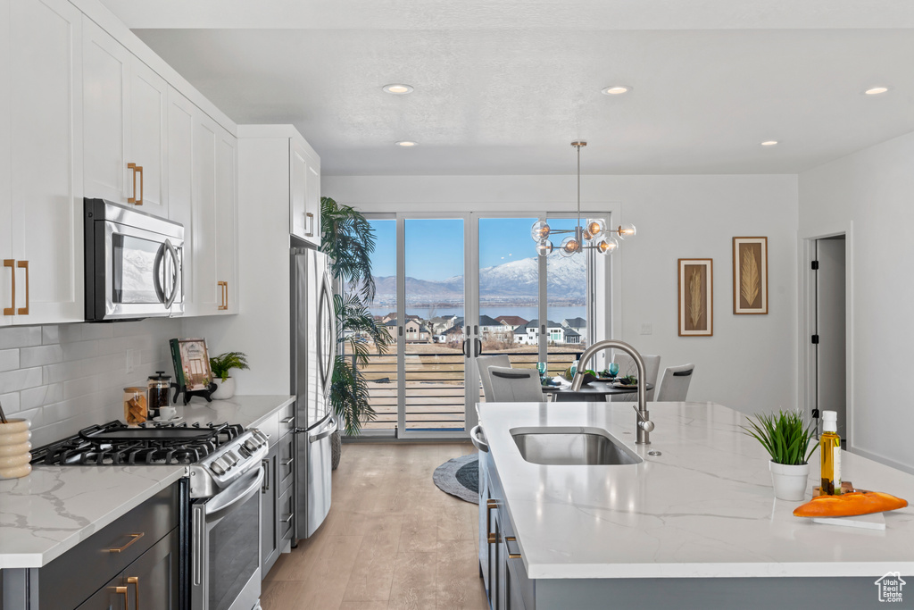 Kitchen with appliances with stainless steel finishes, a mountain view, light wood-style flooring, tasteful backsplash, and white cabinetry