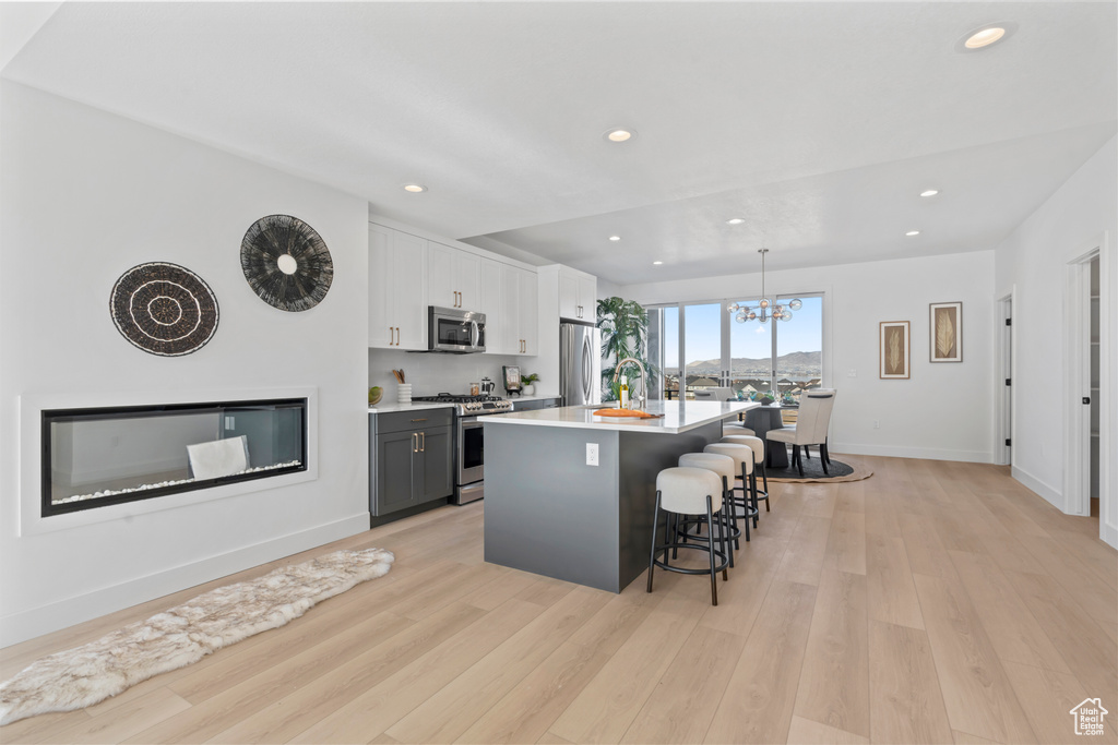 Kitchen featuring appliances with stainless steel finishes, a chandelier, a kitchen breakfast bar, an island with sink, and recessed lighting