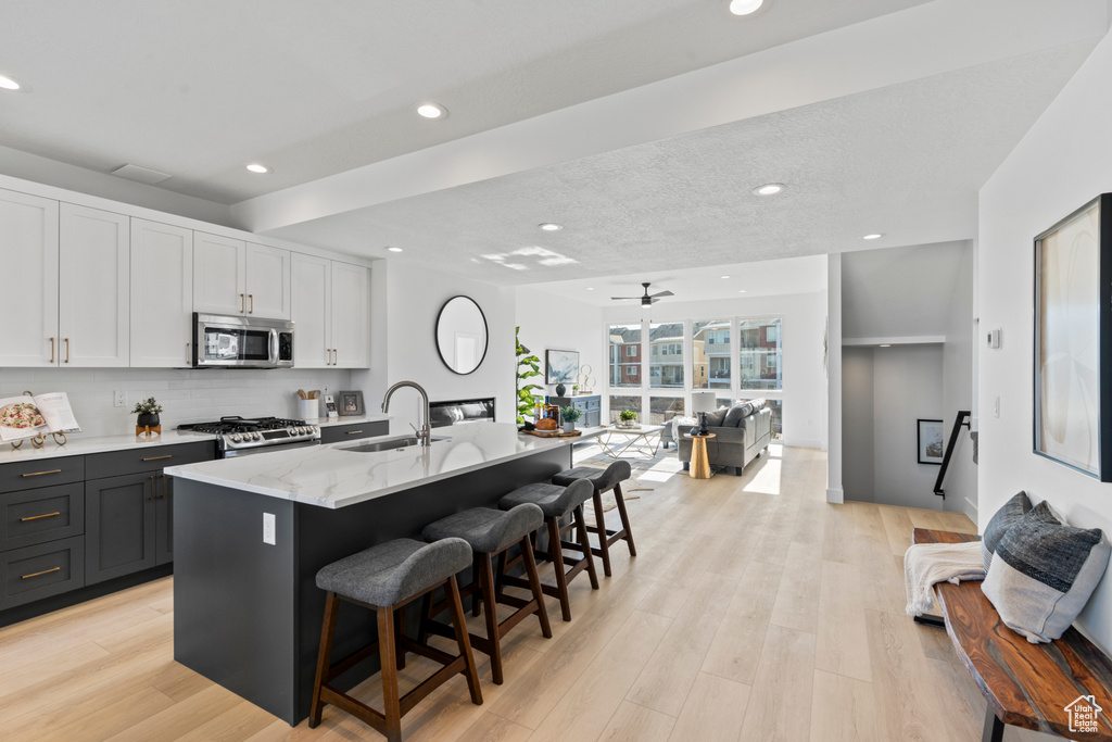 Kitchen with stainless steel appliances, open floor plan, recessed lighting, a kitchen breakfast bar, and light stone counters