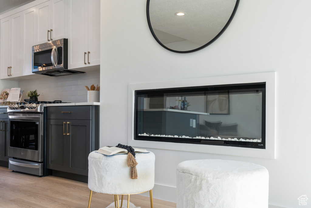 Kitchen with stainless steel appliances, light wood-type flooring, backsplash, white cabinetry, and recessed lighting