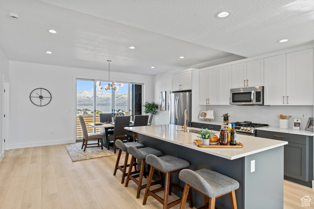 Kitchen featuring stainless steel appliances, recessed lighting, a breakfast bar area, light wood-style floors, and a chandelier