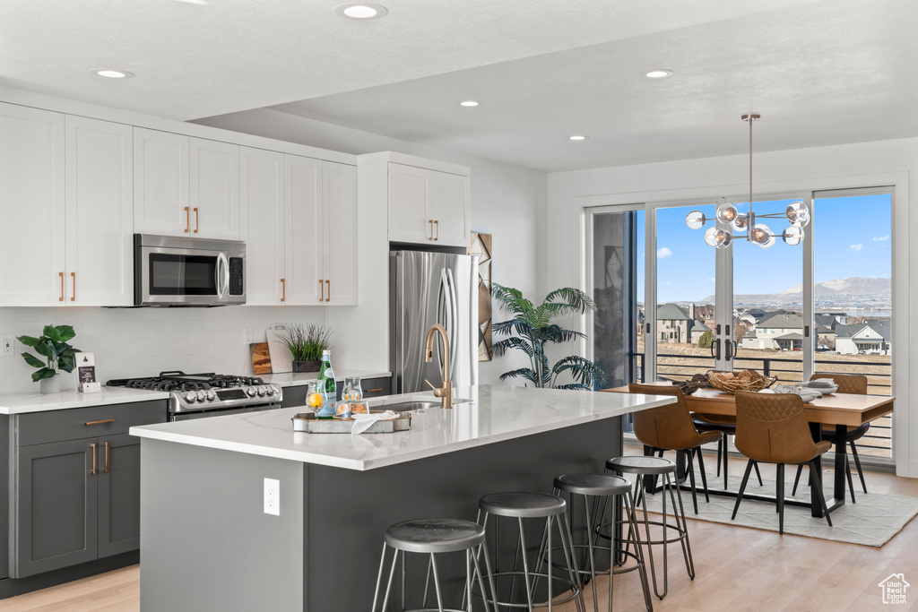 Kitchen with appliances with stainless steel finishes, light wood-style flooring, a kitchen bar, a kitchen island with sink, and recessed lighting