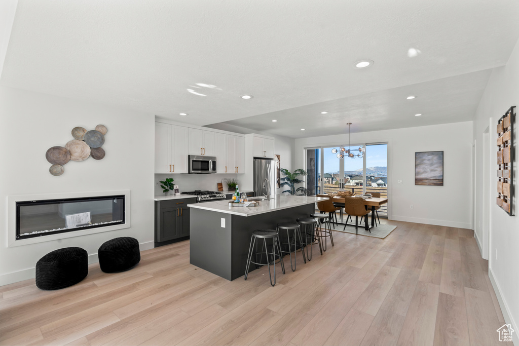 Kitchen with stainless steel appliances, a breakfast bar, light wood-style floors, recessed lighting, and light countertops