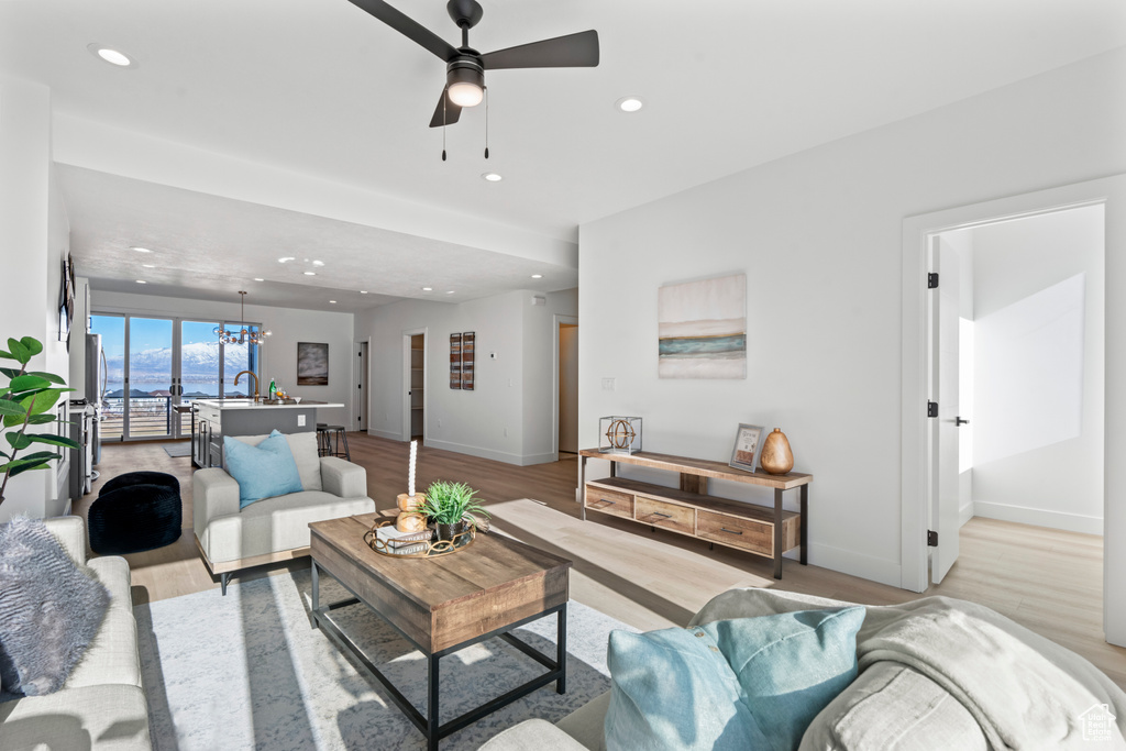 Living room featuring light wood finished floors, ceiling fan, recessed lighting, and a chandelier