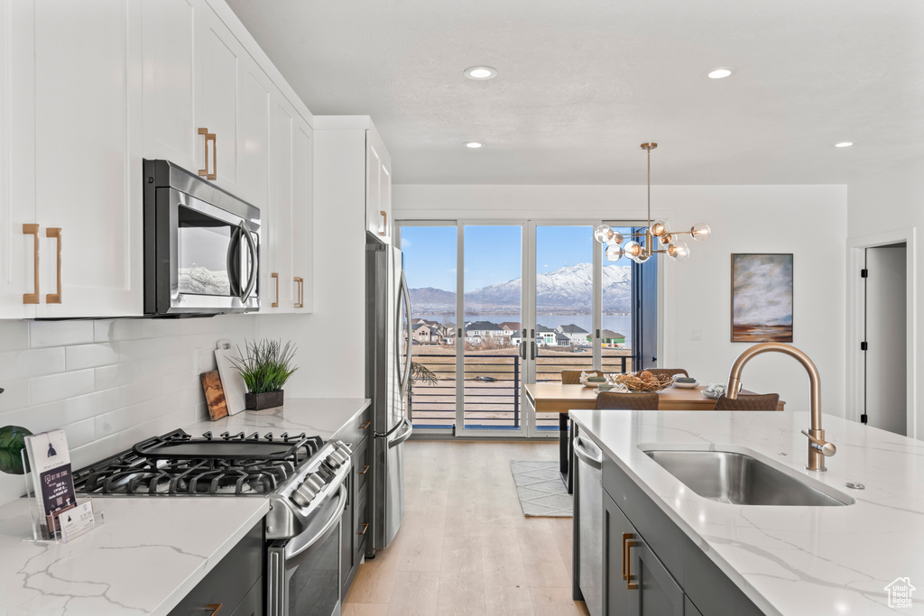 Kitchen featuring stainless steel appliances, a mountain view, white cabinetry, light wood-type flooring, and decorative backsplash