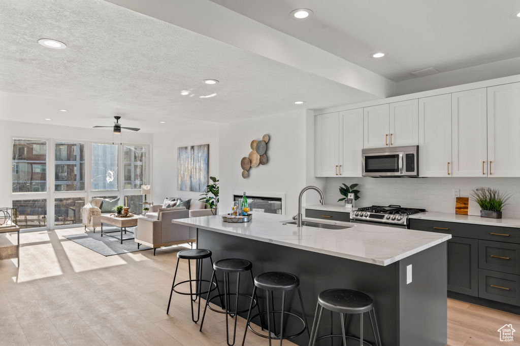 Kitchen with appliances with stainless steel finishes, open floor plan, a kitchen breakfast bar, decorative backsplash, and white cabinetry