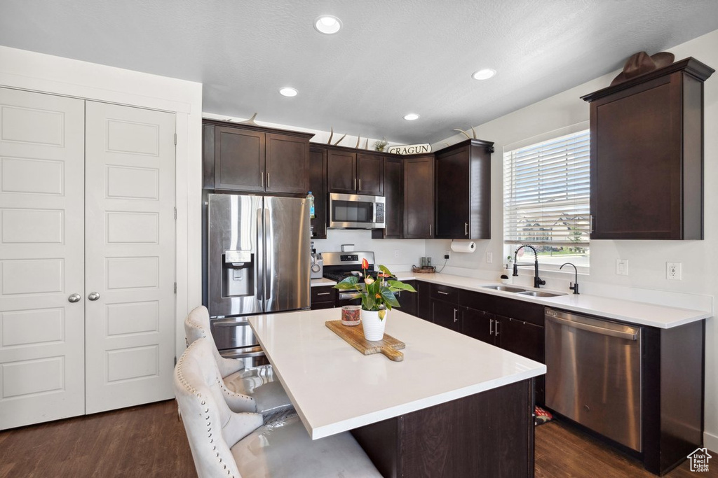 Kitchen with stainless steel appliances, a breakfast bar area, dark brown cabinets, light countertops, and dark wood-style flooring