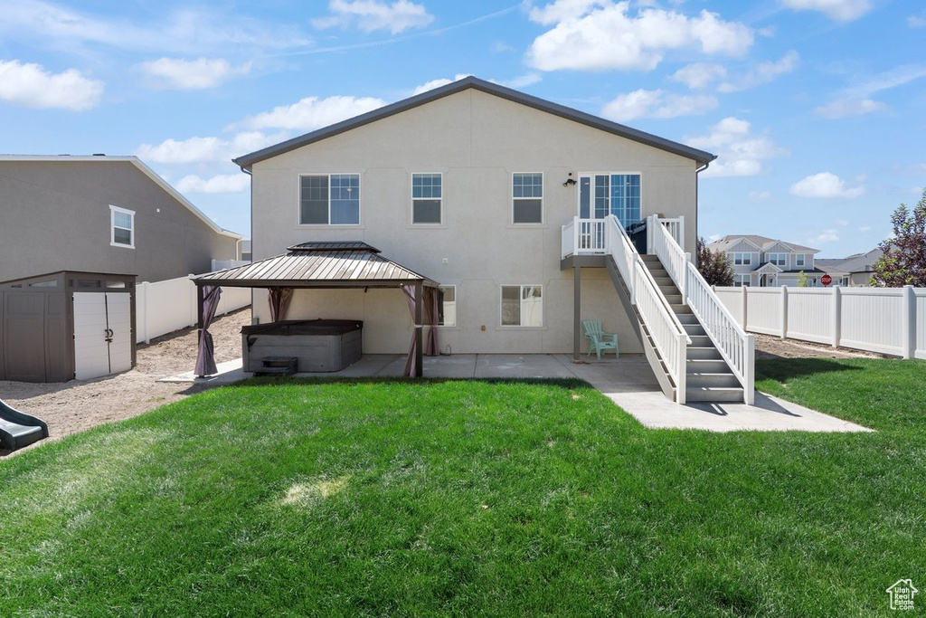 Rear view of property featuring a hot tub, a patio, stucco siding, a fenced backyard, and stairs