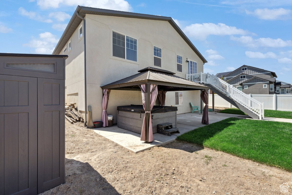 Rear view of house with a hot tub, a patio, a gazebo, stucco siding, and a shed