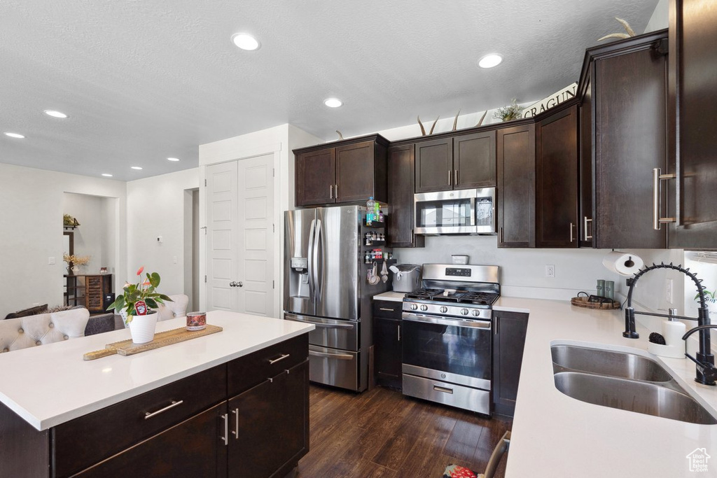 Kitchen featuring stainless steel appliances, light countertops, dark wood-type flooring, dark brown cabinets, and recessed lighting