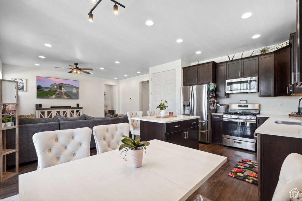 Kitchen with stainless steel appliances, a kitchen island, dark brown cabinetry, dark wood-type flooring, and light countertops