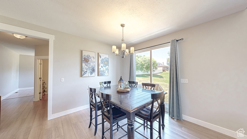 Dining area with a chandelier, light wood-style floors, and a textured ceiling