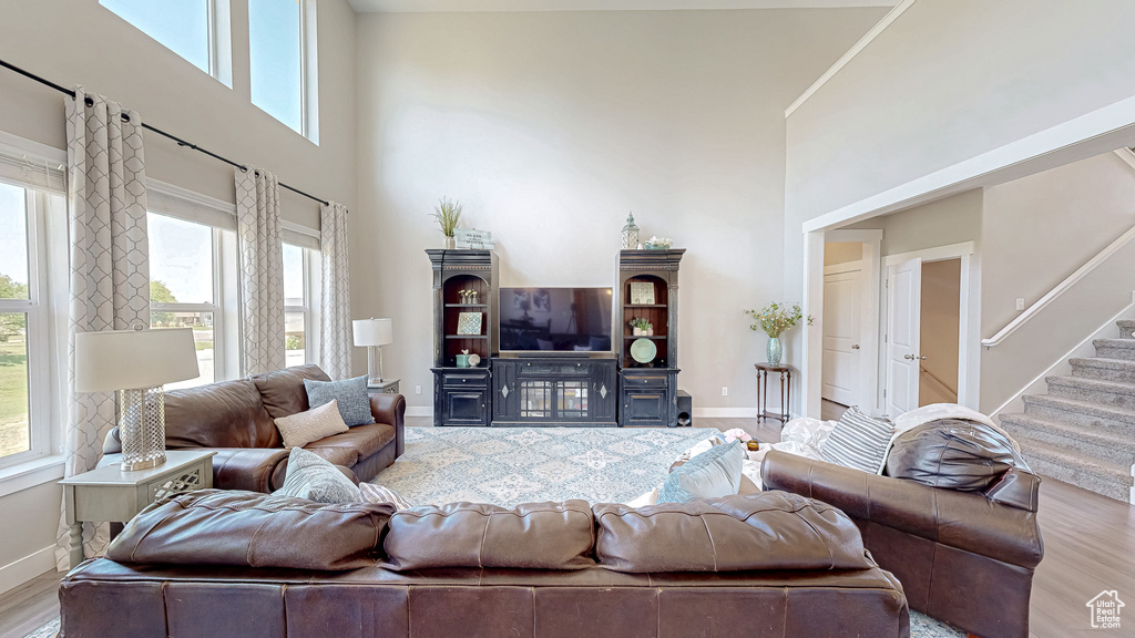 Living area featuring a towering ceiling, healthy amount of natural light, wood finished floors, and stairs