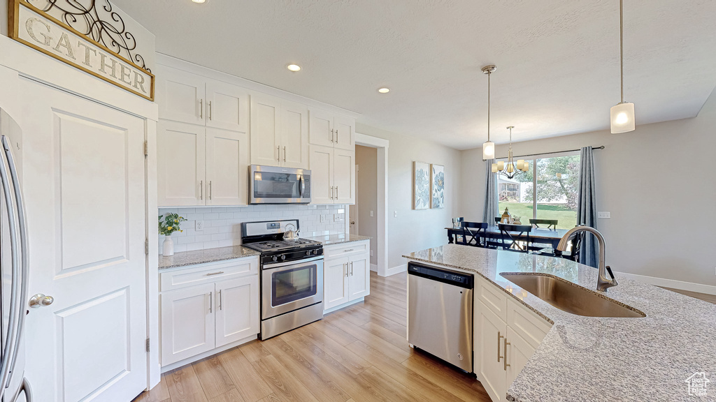 Kitchen featuring stainless steel appliances, backsplash, a chandelier, light wood-style floors, and white cabinets