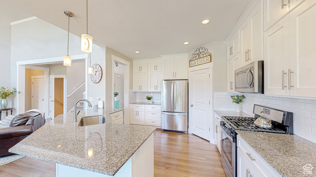 Kitchen with stainless steel appliances, light wood-type flooring, white cabinetry, tasteful backsplash, and recessed lighting