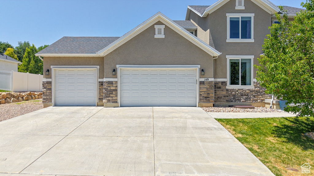 View of front facade with stone siding, stucco siding, concrete driveway, and an attached garage