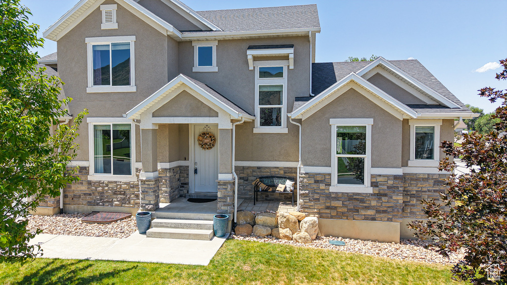 View of front facade featuring stone siding, stucco siding, and roof with shingles