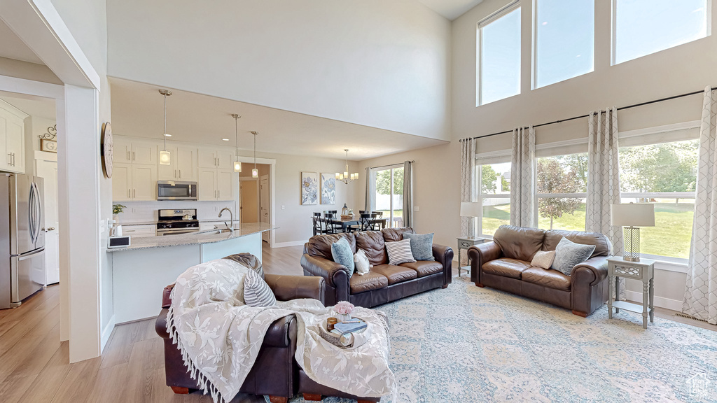 Living area featuring light wood-style flooring, a chandelier, and a towering ceiling