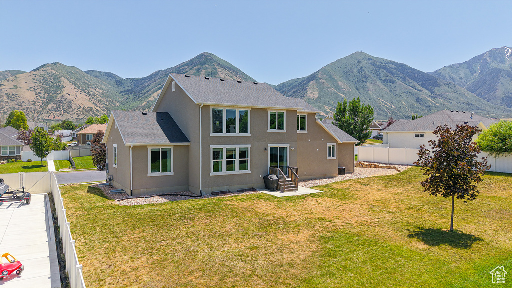 Rear view of house with stucco siding, a fenced backyard, a mountain view, and roof with shingles