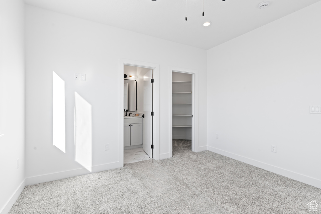 Unfurnished bedroom with a walk in closet, light carpet, connected bathroom, and a closet
