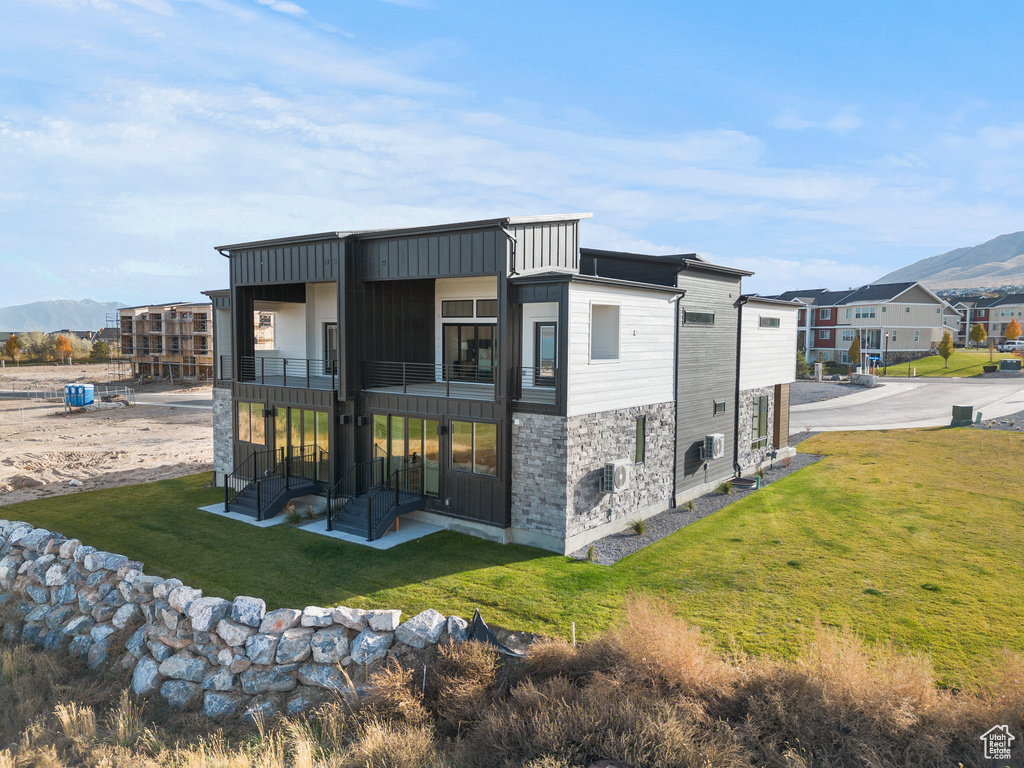Back of house featuring a balcony, a mountain view, a yard, stone siding, and a patio