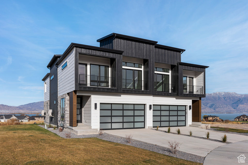 Contemporary home featuring a mountain view, an attached garage, a balcony, a front yard, and concrete driveway
