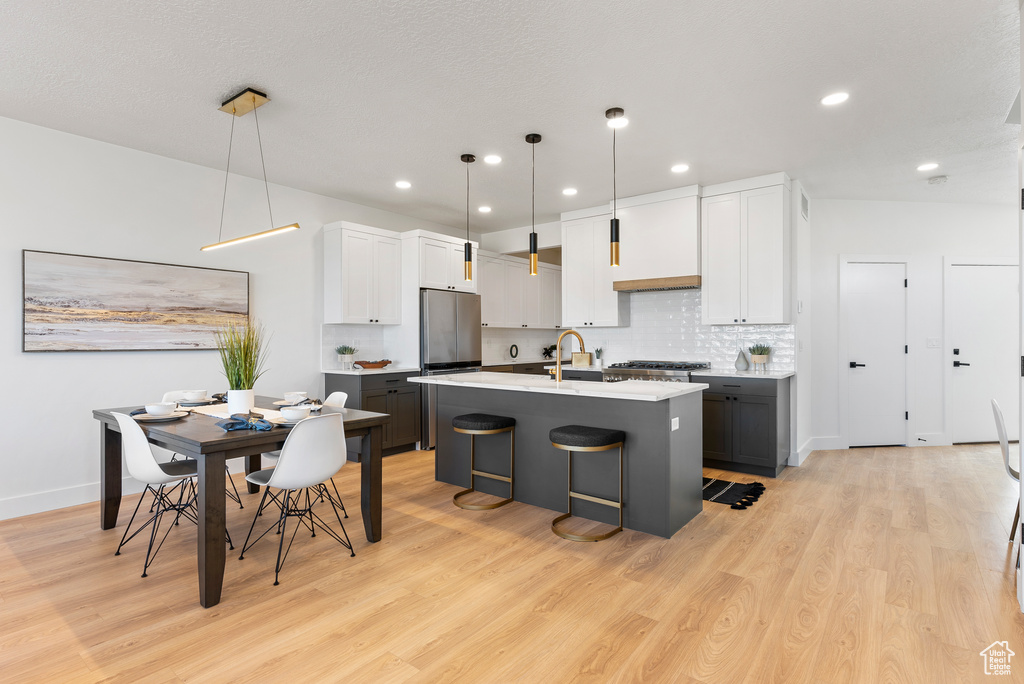 Kitchen featuring freestanding refrigerator, light countertops, light wood-type flooring, an island with sink, and recessed lighting