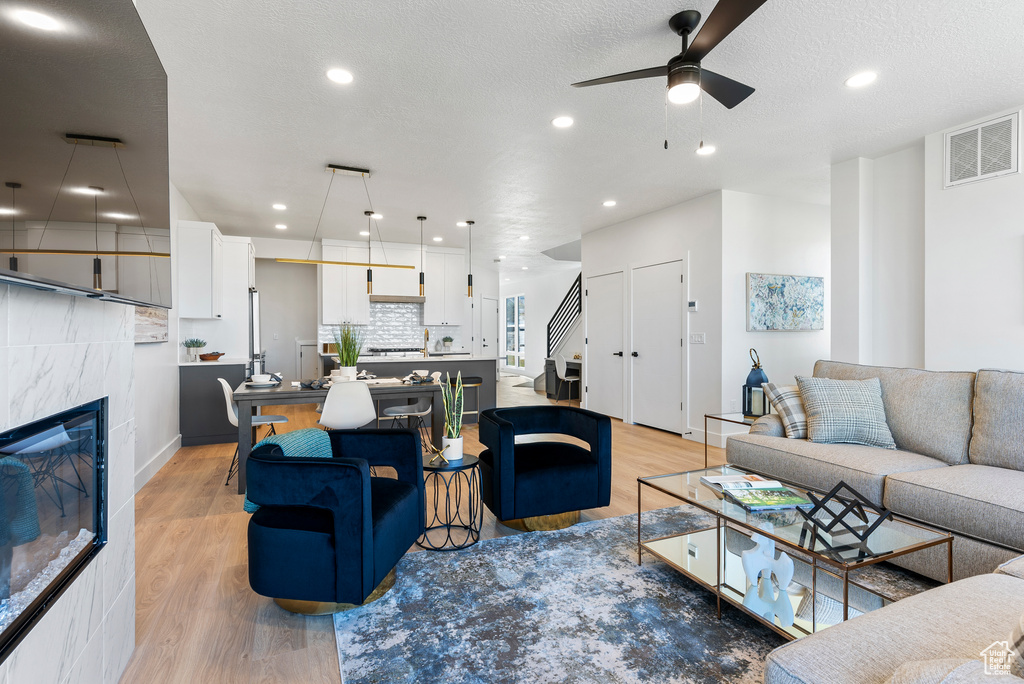Living area featuring ceiling fan, light wood finished floors, a tile fireplace, recessed lighting, and baseboards