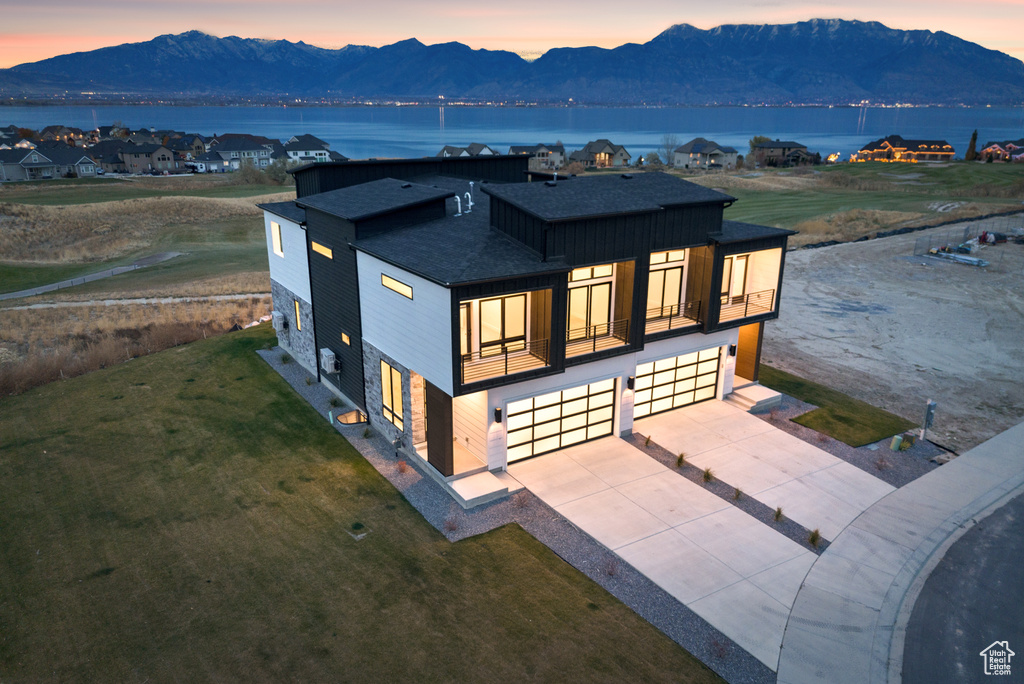 Rear view of house featuring a shingled roof, a garage, a balcony, concrete driveway, and a yard