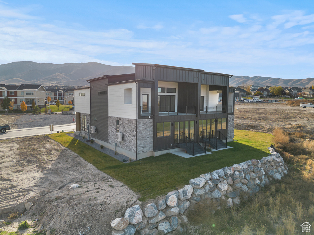 Back of house with a mountain view, stone siding, a balcony, and a yard