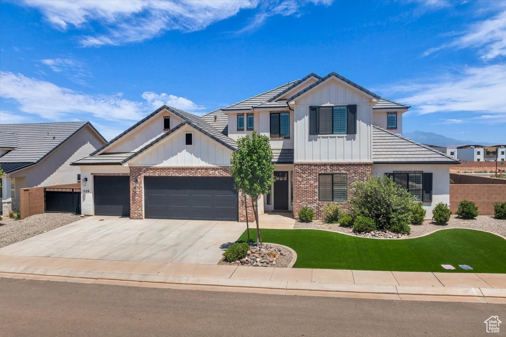 Modern farmhouse style home with board and batten siding, brick siding, driveway, a garage, and a tiled roof