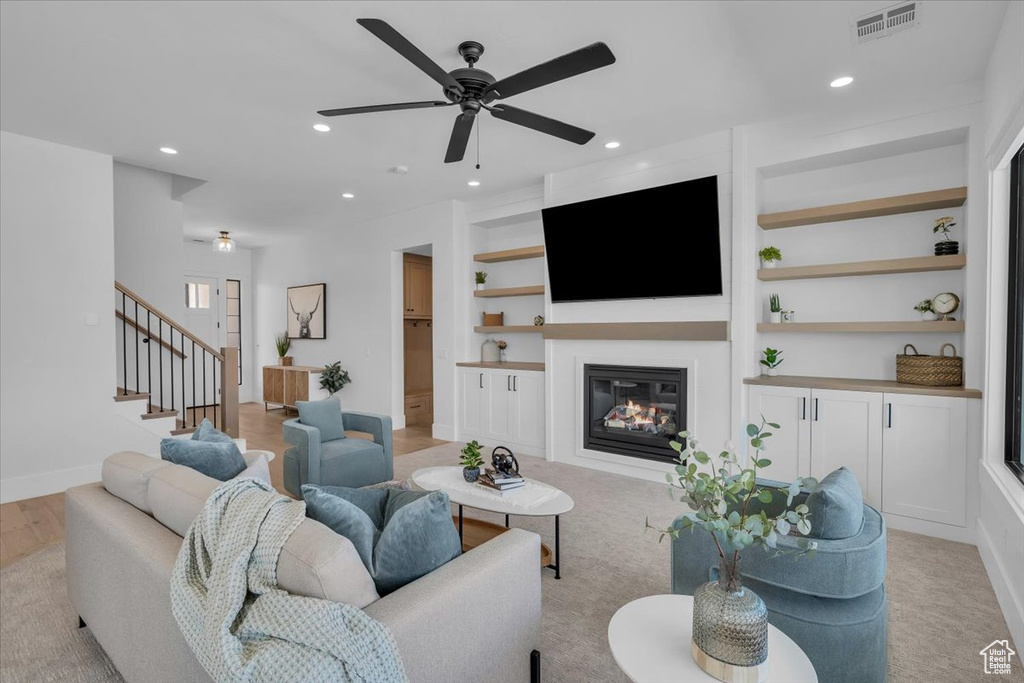 Living area with a glass covered fireplace, built in shelves, a ceiling fan, recessed lighting, and stairway