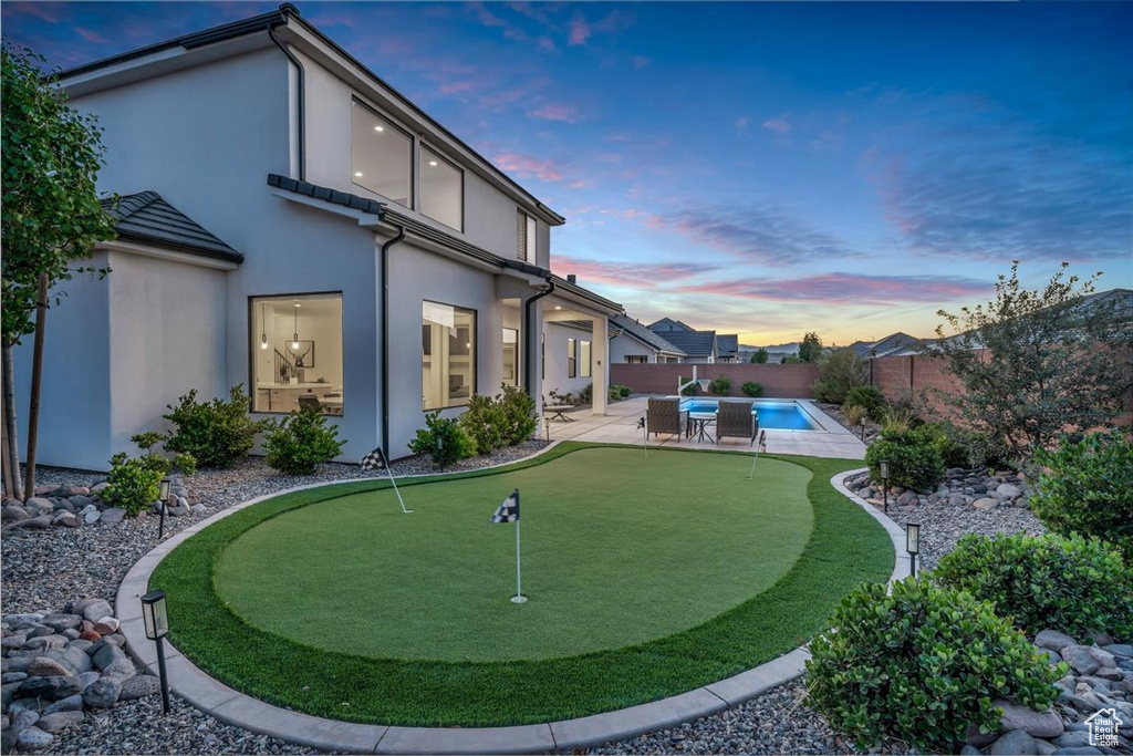 Back of house at dusk with a putting green, a patio, a fenced backyard, and stucco siding