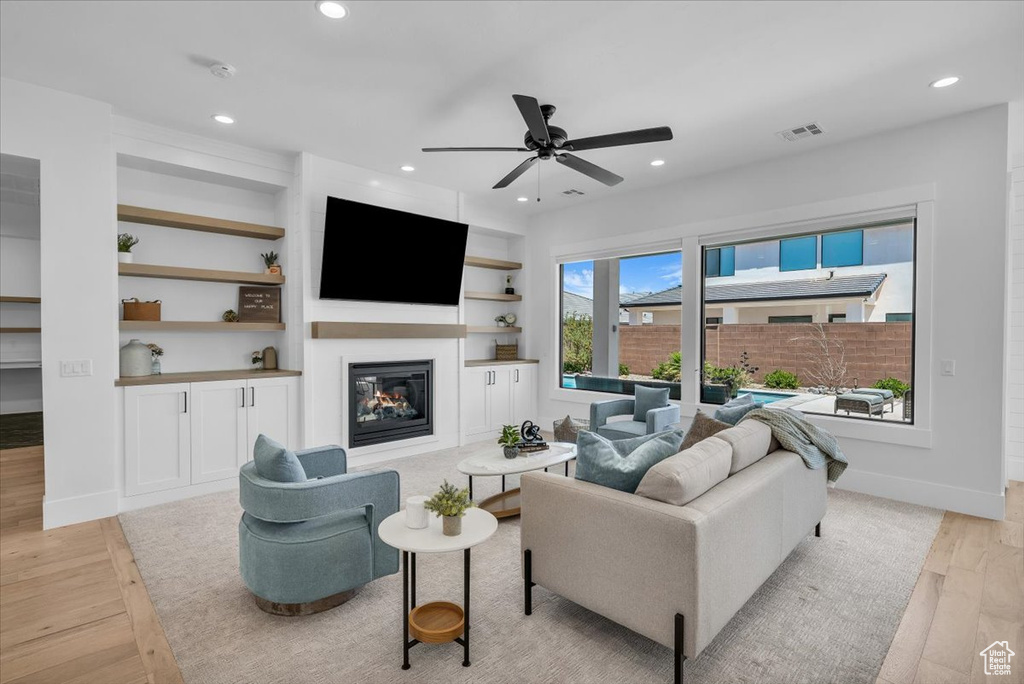 Living room featuring light wood-style floors, recessed lighting, a glass covered fireplace, ceiling fan, and built in features