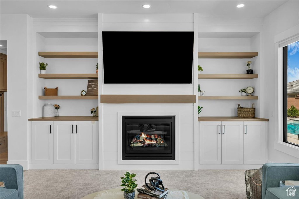 Living area featuring built in features, a glass covered fireplace, carpet flooring, and recessed lighting