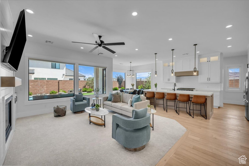 Living room with recessed lighting, light wood-type flooring, ceiling fan, a glass covered fireplace, and a chandelier