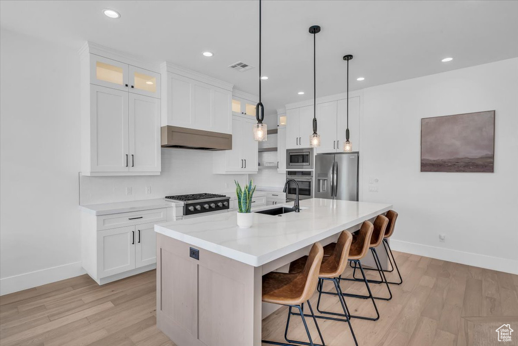 Kitchen with stainless steel appliances, light wood finished floors, white cabinets, range hood, and recessed lighting