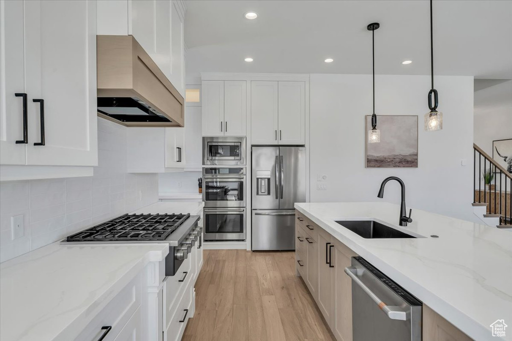 Kitchen featuring stainless steel appliances, custom exhaust hood, light stone counters, light wood-style floors, and white cabinetry