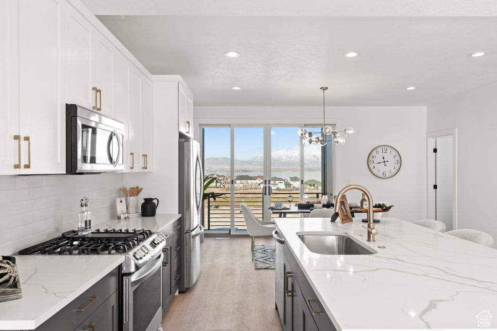 Kitchen with appliances with stainless steel finishes, light wood-style floors, white cabinets, tasteful backsplash, and recessed lighting