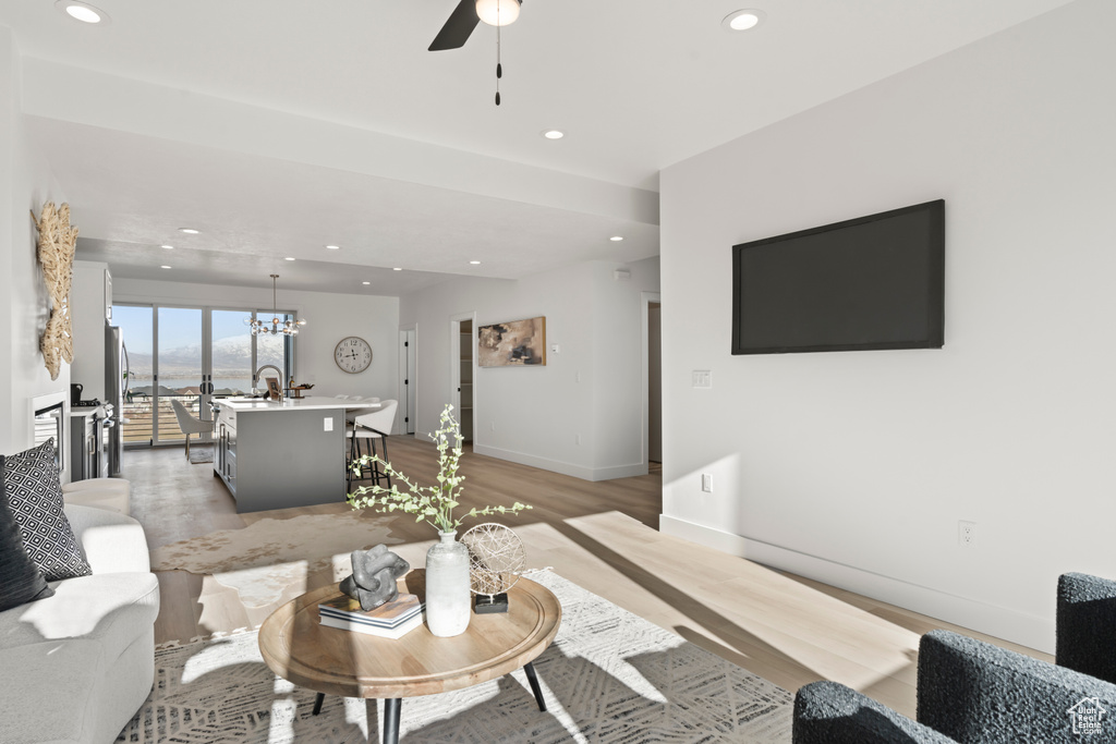 Living area with light wood-style floors, recessed lighting, ceiling fan, and a chandelier