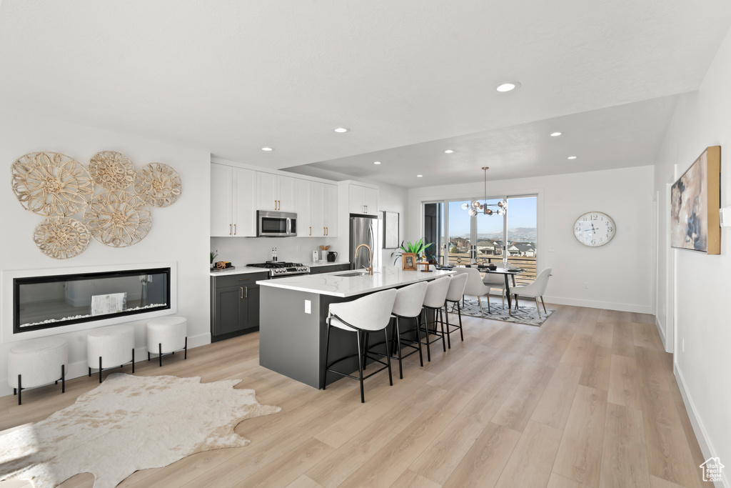 Kitchen featuring stainless steel appliances, a breakfast bar, a chandelier, a center island with sink, and light wood-style flooring