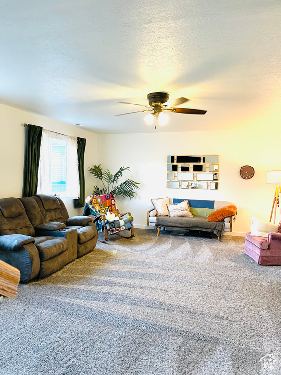 Carpeted living area featuring a ceiling fan and baseboards
